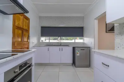 a kitchen with white cabinets and a sink and a window at Greencroft Villa in Kempton Park
