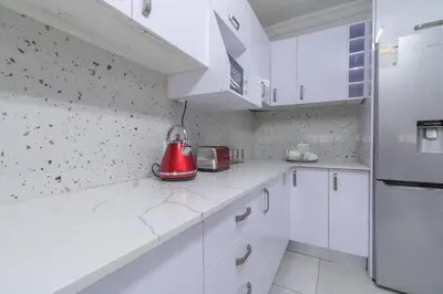 a white kitchen with white cabinets and a red appliance at Greencroft Villa in Kempton Park