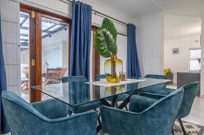 a dining room with a glass table and blue chairs at Greencroft Villa in Kempton Park