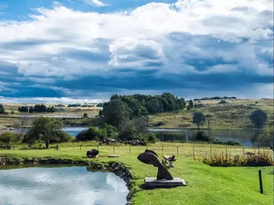 a pond in a field next to a body of water at Kinloch Lodge in Dullstroom