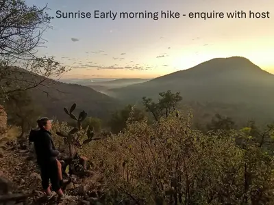 a man sitting on a hill looking at the mountains at Rustic Unique - Bush Glamping Retreat in Kalkheuvel