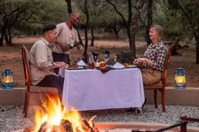 a group of people sitting around a table next to a fire at Sable Ranch Bush Lodge in Brits