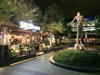 a statue of a woman in front of a restaurant at night at Luxury 1 bedroom apartment in vibrant Menlyn Maine in Pretoria