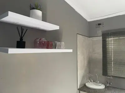 a bathroom with white shelves with vases on the wall at Solace Unit in Phalaborwa