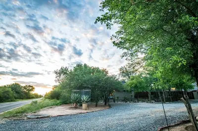 a house with a gravel driveway with trees and a street at Nkanyi Wildlife House & Cottage in Hoedspruit