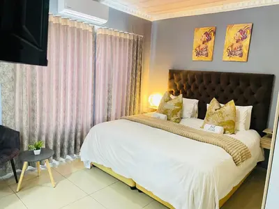 a bedroom with a large bed with white sheets and gold pillows at Mnqobi Lifestyle Apartments in Nelspruit