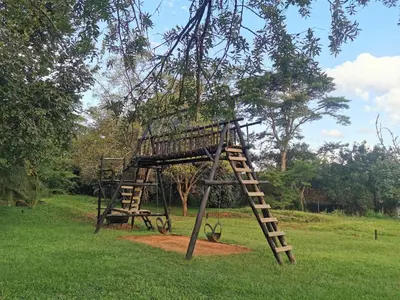 a wooden play structure in a field with a tree at The Bird Hide Luxury Self catering Chalets in White River