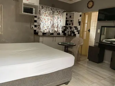 a bedroom with a bed and a table and a kitchen at northmead lodge in Benoni