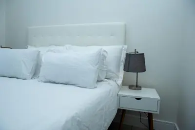 a white bed with white pillows and a lamp on a night stand at Fealathome Apartment in Midrand