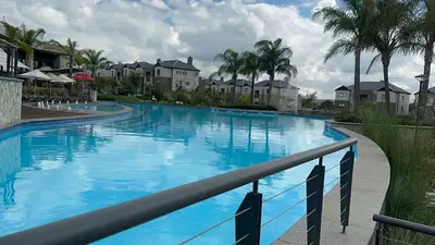a large blue swimming pool with palm trees and houses at Fealathome Apartment in Midrand