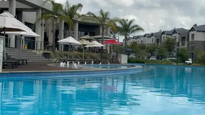 a swimming pool with chairs and umbrellas next to a building at Fealathome Apartment in Midrand