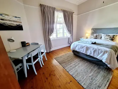 a bedroom with a bed and a desk and a window at Oude Post Guesthouse and Cottage - The Old Postmaster's House in Lydenburg
