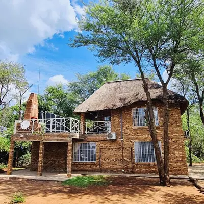 a brick house with a thatched roof and a tree at Bliss in Marloth Park