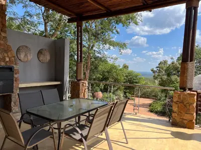 a patio with a glass table and chairs on a balcony at Pumula Bush Chalet in Mabula