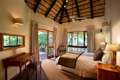 a bedroom with a bed and a desk and windows at Kruger Park Lodge unit 34 in Hazyview