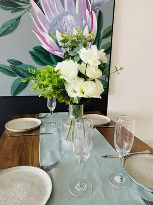 a vase of flowers on a table with plates and glasses at Ellipse Waterfall Luxury Apartments in Midrand