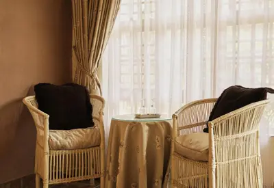 two wicker chairs and a table in front of a window at Villa Ticino Guest House in Sabie