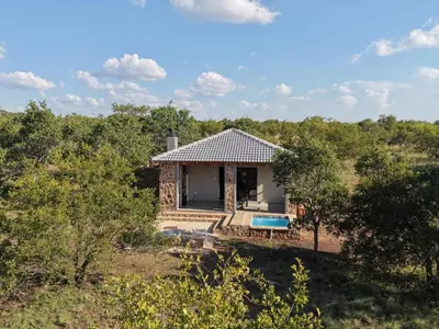 a cottage in the middle of a field with trees at Klipdrift Sands Game Lodge in Dinokeng Game Reserve