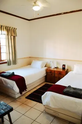 a bedroom with two beds and a table and a window at Machado Stay Pecan Cottage 1 in Machadodorp