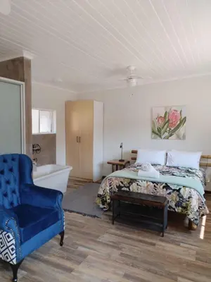 a bedroom with a bed and a blue chair and a tub at Lodge Laske Nakke in Lydenburg