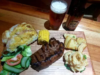 a plate of food with meat and vegetables and a drink at Lodge Laske Nakke in Lydenburg