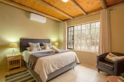 a bedroom with a bed and a window and a chair at Kudus Crest Bush Retreat in Marloth Park