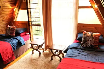 a bedroom with two beds and two windows at Serenity Graskop, 3 bedroom A-Frame cottage in Graskop