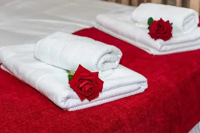 three white towels with red roses on a bed at Roosthaven Guesthouse in Centurion