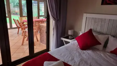 a bedroom with a bed with red pillows and a balcony at Roosthaven Guesthouse in Centurion