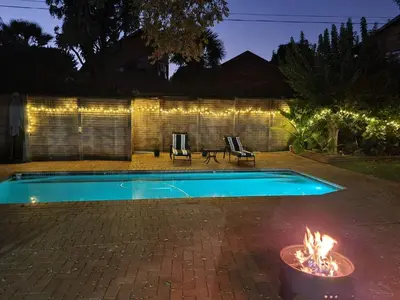 a swimming pool with a fire in a backyard at night at Roosthaven Guesthouse in Centurion